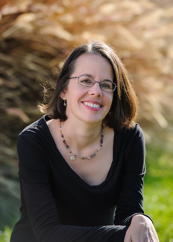 Woman with short brown hair, smiling, wearing glasses and a necklace